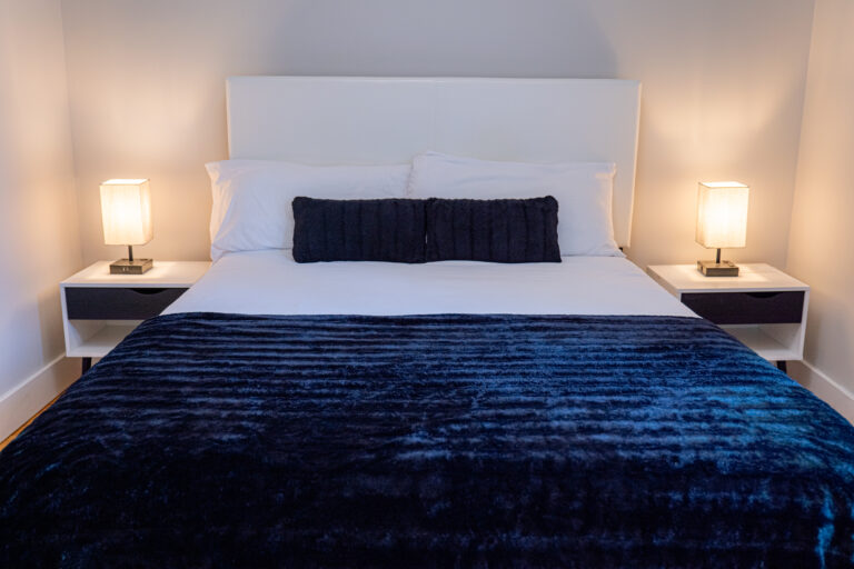 Neatly made bed with navy blue blanket, matching pillows, and soft lighting in a comfortable Ocean Hill unit.