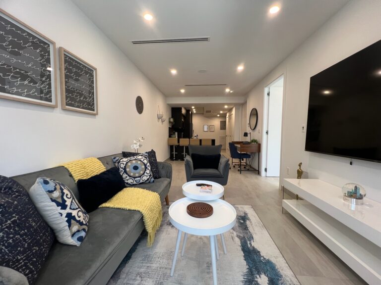 Spacious living room with modern decor, white coffee tables, and view into kitchen and work area in Greenpoint, NYC.
