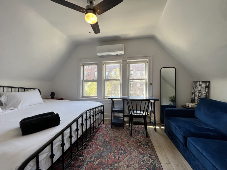 Bedroom with a black metal bed, white bedding, and a blue sofa, featuring a ceiling fan and artwork on the wall.