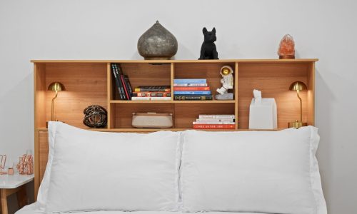Wooden headboard with built-in shelves holding books, decor items, and bedside lamps above a neatly made bed.