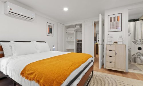 Spacious bedroom with a neatly made bed, open closet displaying folded towels and clothes, and modern decor.