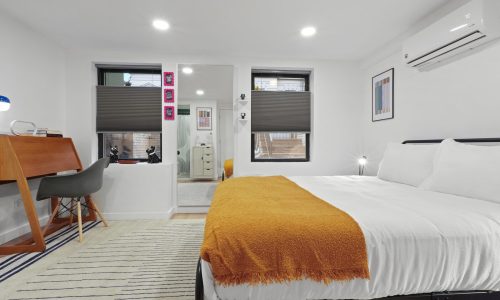 Comfortable bedroom with a black-framed bed, yellow throw blanket, striped rug, and small desk near the window.