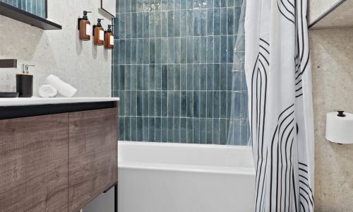 Clean bathroom with a bathtub, blue-tiled wall, black-and-white shower curtain, floating shelves, and modern fixtures.