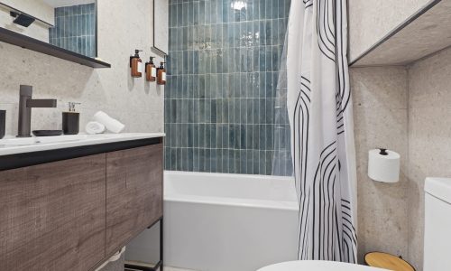 Modern bathroom with a sink vanity, dark faucet, floating shelves, toilet, and striped shower curtain.