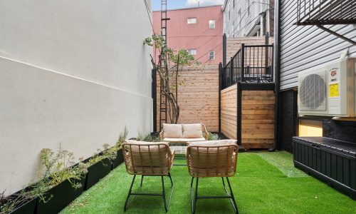 Chic 2BD/2BA in Williamsburg - Compact outdoor space with wicker chairs, sofa, black railings, and wooden fence.