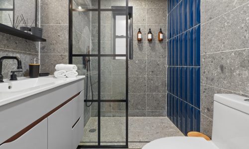 Minimalist bathroom featuring a white sink vanity, black faucet, glass shower enclosure with dark frames, and blue accent tiles.