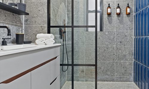 Clean bathroom with a white sink, black faucet, floating shelves, toilet, and gray floor mat.