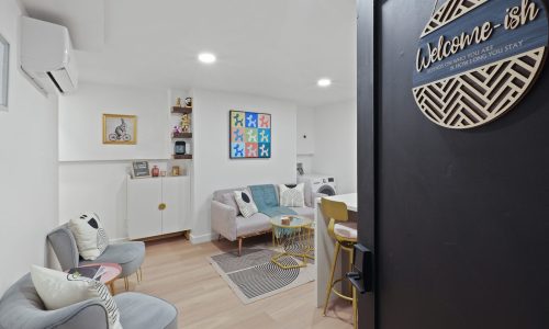 Modern living room with gray sofa, colorful art, welcome sign, and built-in storage.
