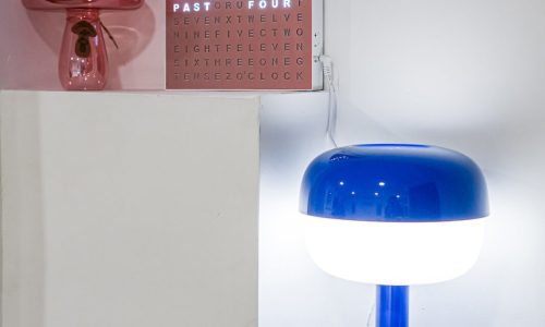Nightstand with a blue lamp and a digital clock displaying the time in colorful letters against a red background.