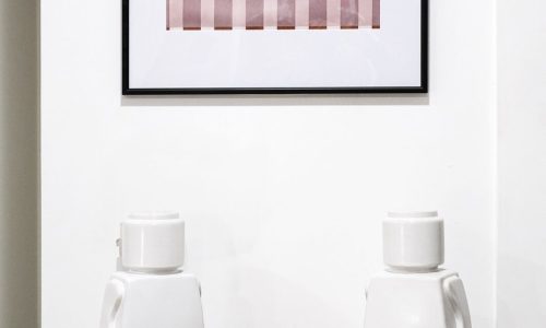 Cabinet with framed abstract artwork above, two white Lego-like figures, a black candle container, and a tray of incense sticks.