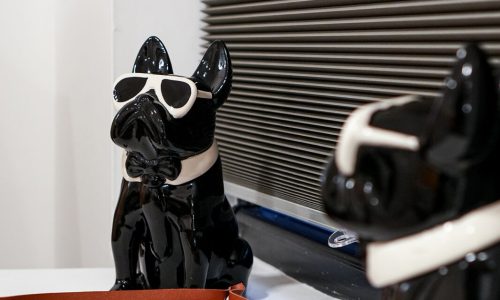 Glossy black dog figurine wearing sunglasses and bow tie, sitting on a red tray.