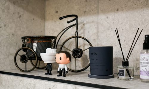 Elegant room countertop with miniature bicycle, figurine, black candle, reed diffuser, and lavender air freshener.