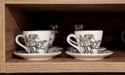 Wooden shelf displaying white coffee cups with black illustrations of royal characters.