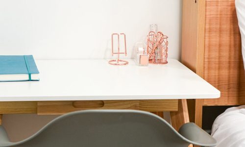 Minimalist desk setup with a blue notebook, pink candle holder, and geometric decor beside a gray chair.